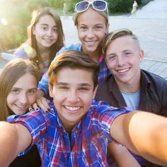 Fünf Jugendliche posieren im Freien lachend gemeinsam für ein Selfie.