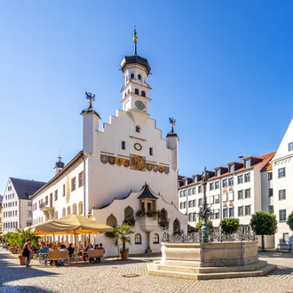 Rathausplatz in Kempten mit Brunnen, Rathaus und umliegenden Gebäuden unter blauem Himmel.