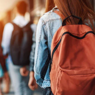 Mehrere junge Menschen mit Rucksäcken gehen in unscharfer Aufnahme durch einen hellen Außenbereich oder Flur.